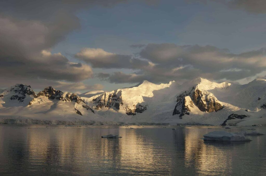 Dusk and flat calm water off the shore of a mountain landscape in Antarctica.